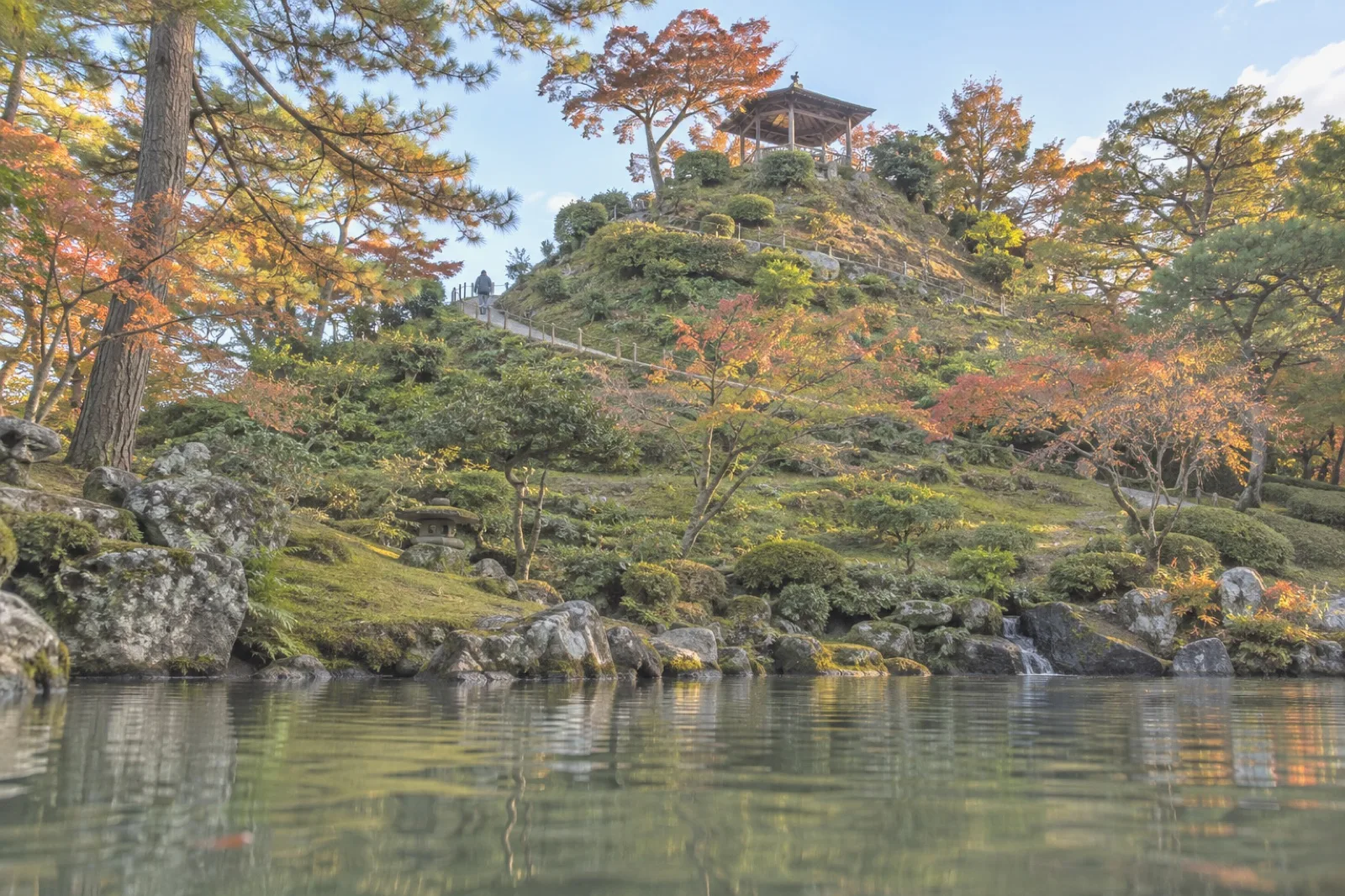 A spiral hill with an arbour at its summit, a pond in the foreground